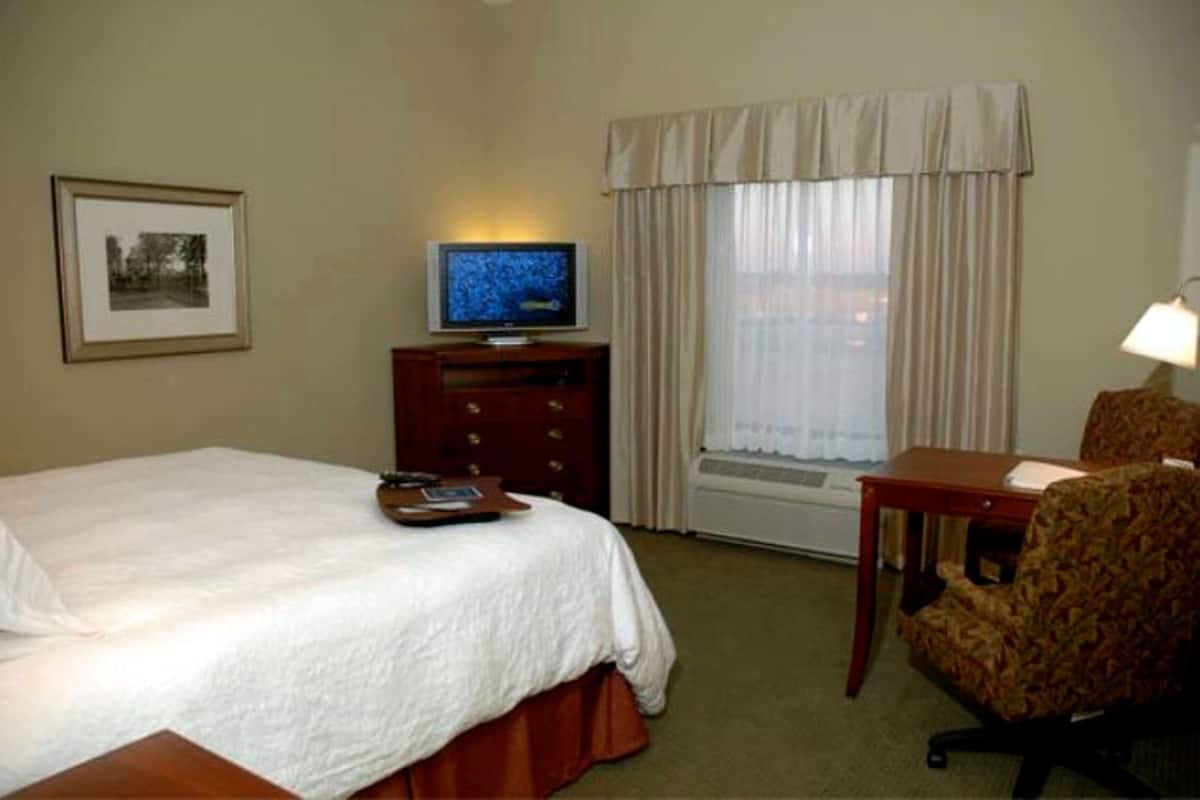 A hotel room with a bed, a television, a desk, a chair, and a window with curtains.