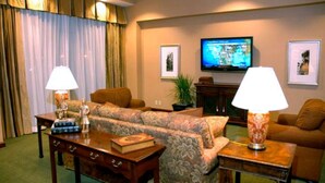 A hotel living room with a sofa, two lamps, a television, and framed pictures on the wall.