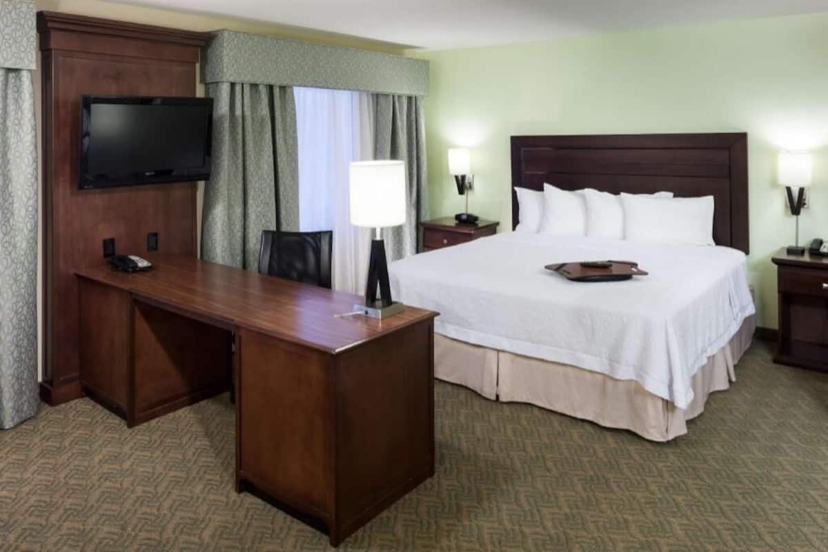 A hotel room with a bed, a desk with a chair, a television, and two bedside lamps.