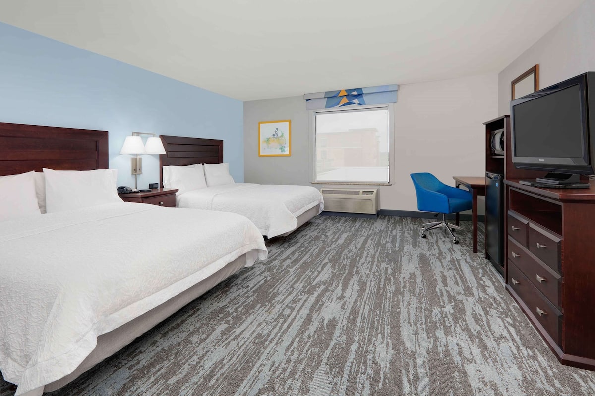A hotel room with two beds, a desk, a chair, a television, and a window with a view.