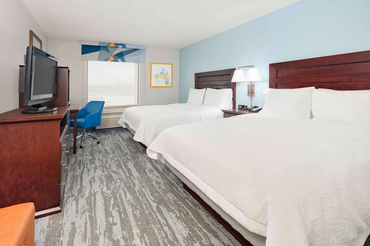 A hotel room with two beds, a desk with a television, a chair, and a window with a view.