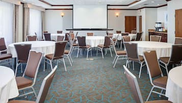 Una sala conferenze con tavoli e sedie rotonde, uno schermo per proiettore e un pavimento rivestito di moquette.