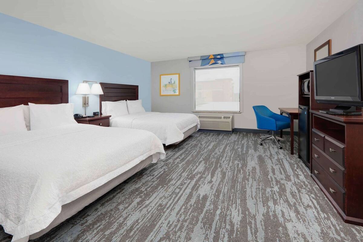 A hotel room with two beds, a desk, a television, and a window.