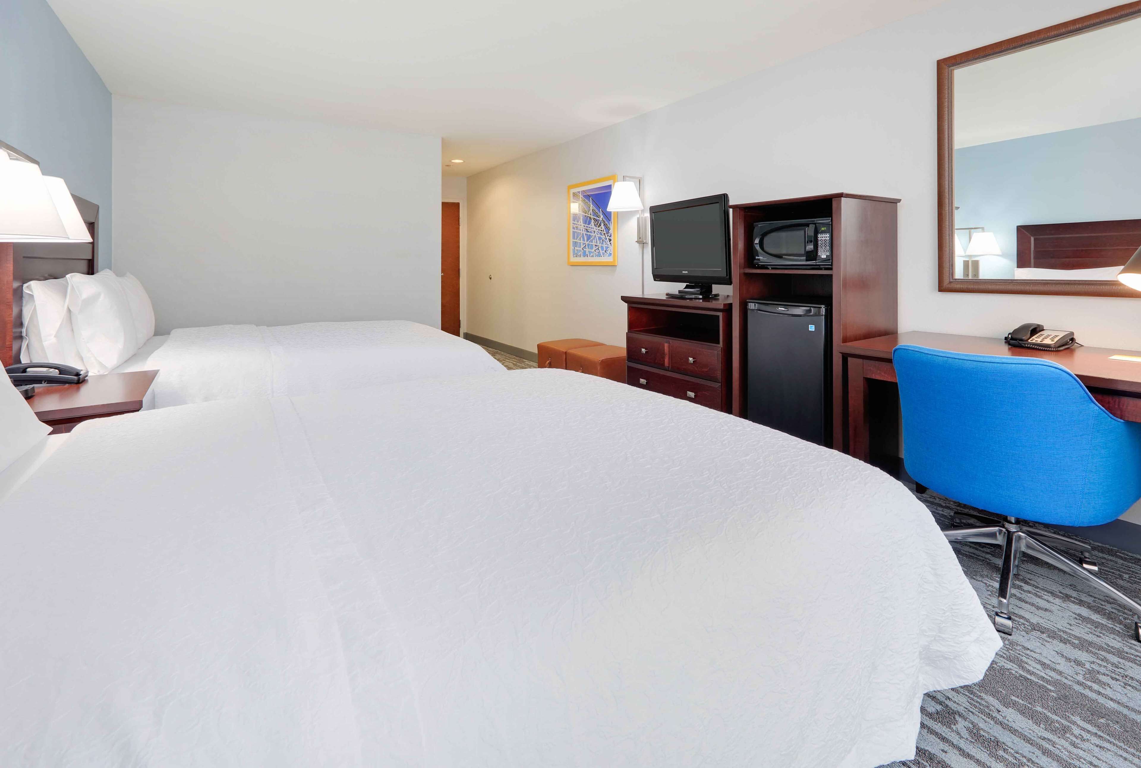A hotel room with two beds, a desk with a chair, a television, a microwave, and a telephone.