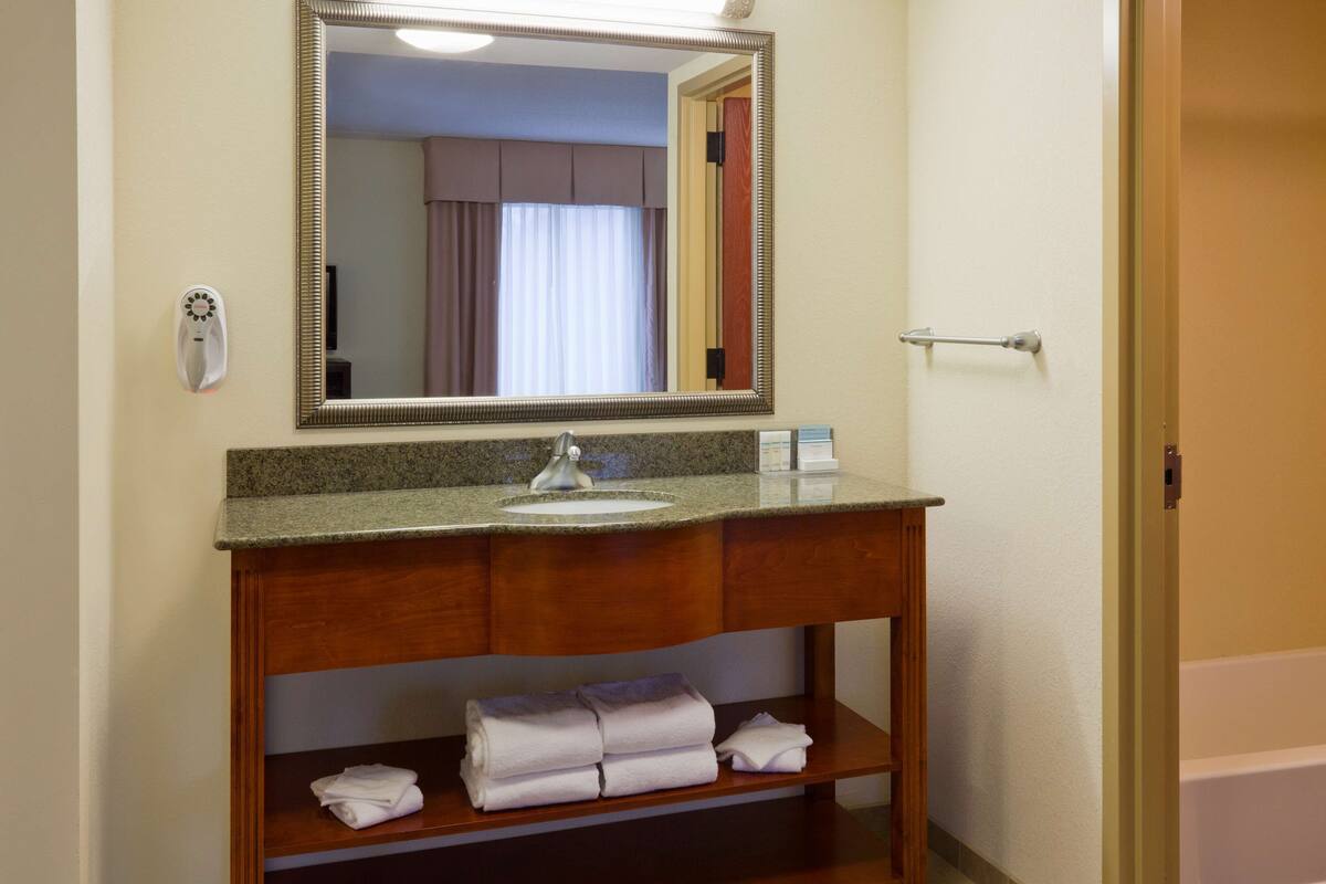 A bathroom with a wooden vanity, a sink, a mirror, and a towel rack with folded towels.