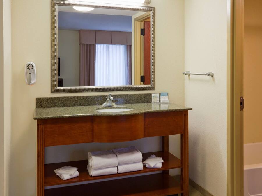 A bathroom with a wooden vanity, a sink, a mirror, and a towel rack with folded towels.