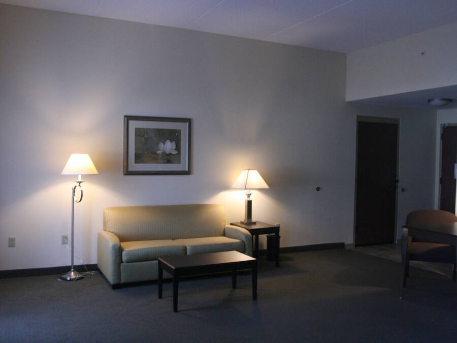 A hotel room with a sofa, two lamps, a small table, and a door leading to another room.
