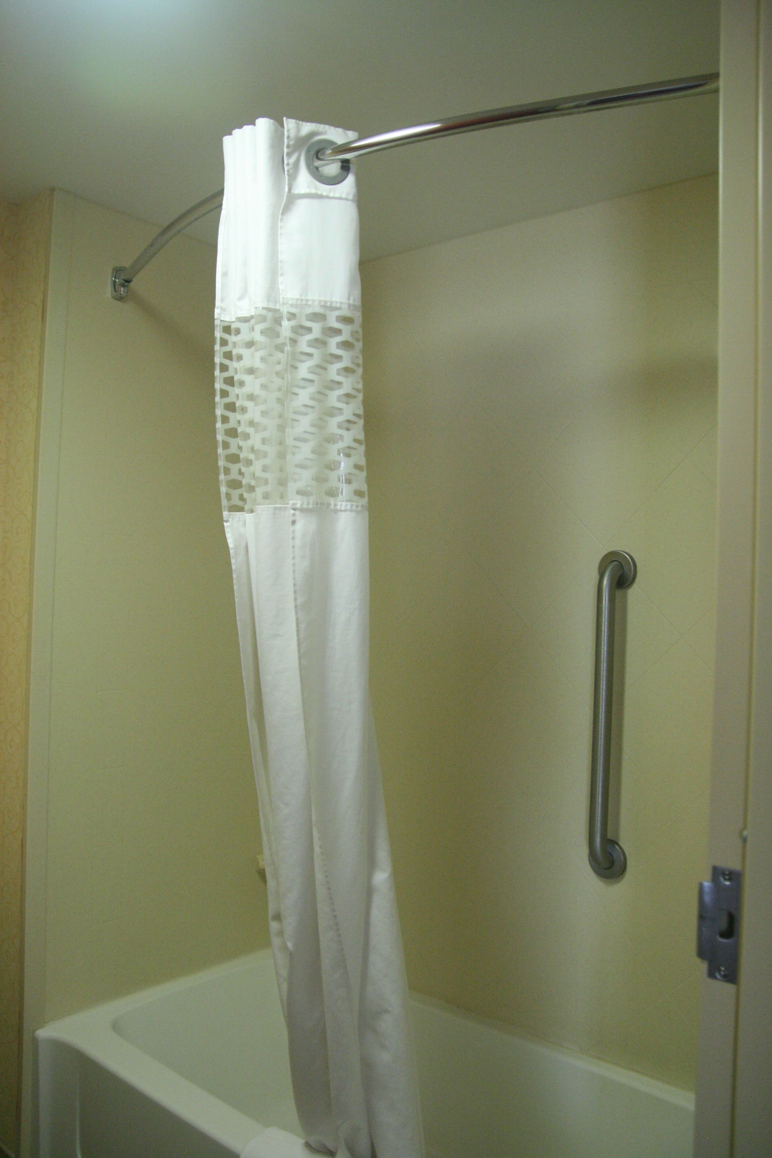 A shower with a white curtain, a grab bar, and a white bathtub.