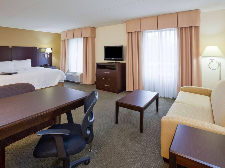 Ett hotellrum med en säng, ett skrivbord, en stol, en tv, en soffa och en lampa.