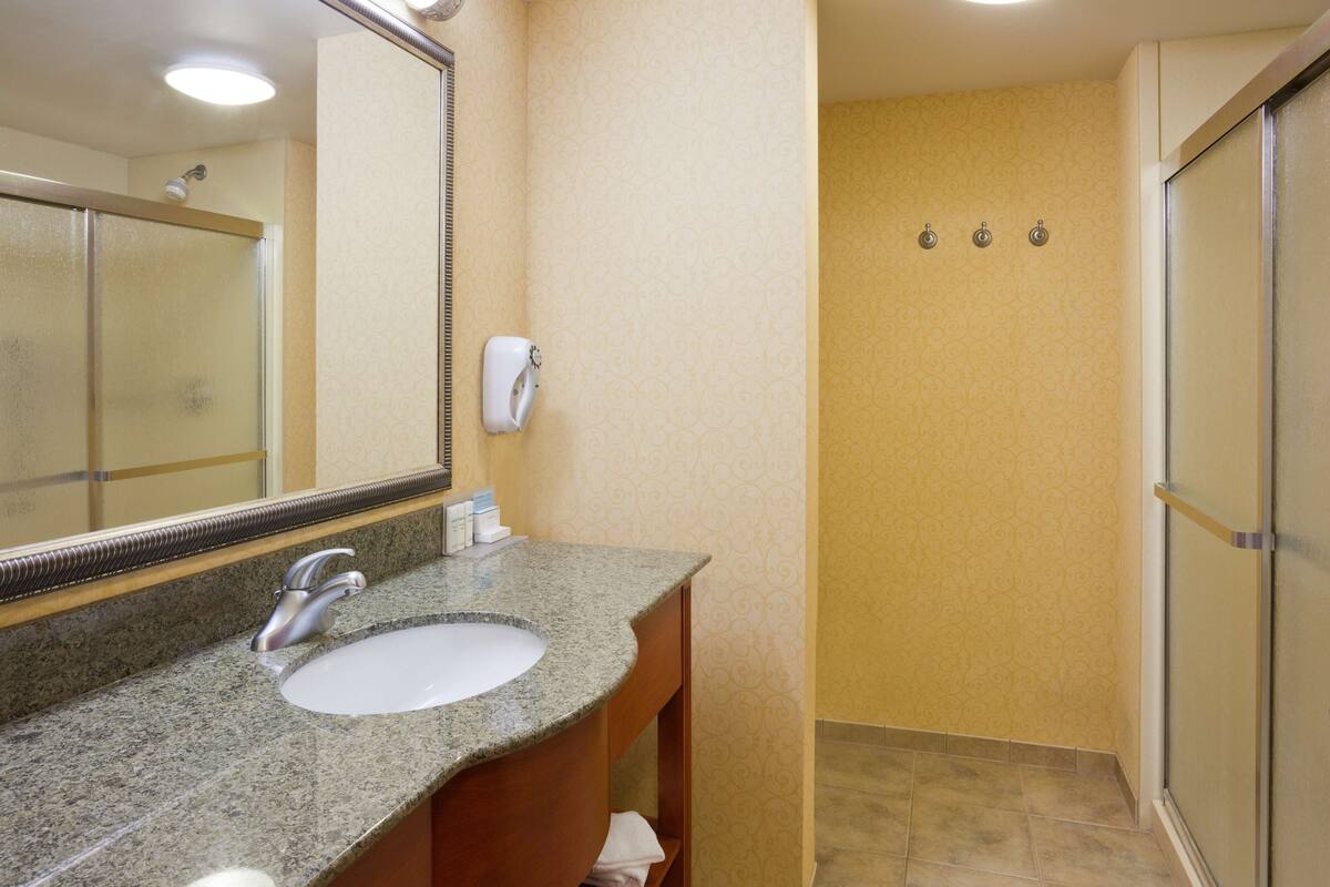A bathroom with a granite countertop sink, a mirror, and a shower area with a glass door.