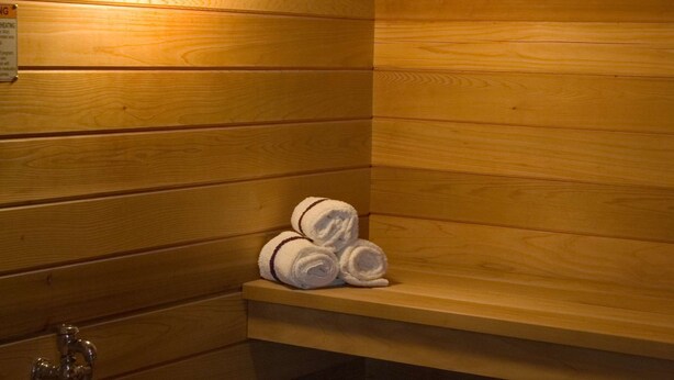 A wooden sauna room with a bench, a shelf with towels, and a bucket with a ladle. - Hampton Inn & Suites Lino Lakes (Circle Pines)