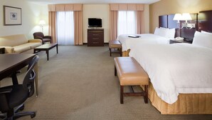 A hotel room with a large bed, a desk with a chair, a sofa, a TV, and a lamp. - Hampton Inn & Suites Lino Lakes (Circle Pines)
