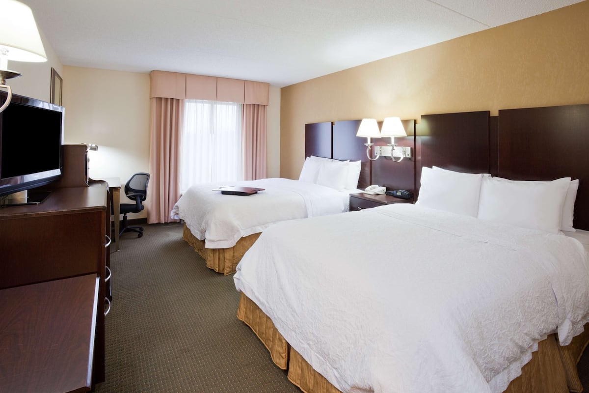 A hotel room with two beds, a desk with a television, and a chair.