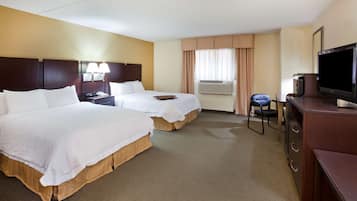 A hotel room with two beds, a desk with a television, and an air conditioning unit.