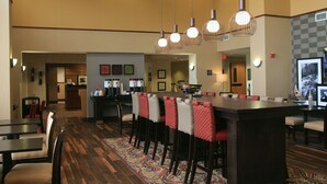 A hotel lobby with a long communal table, multiple chairs, and hanging pendant lights. - Hampton Inn & Suites Lino Lakes (Circle Pines)