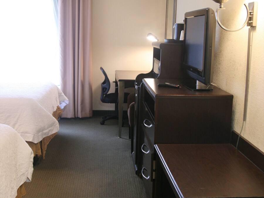 A hotel room with a bed, a desk with a television, a chair, and a lamp.