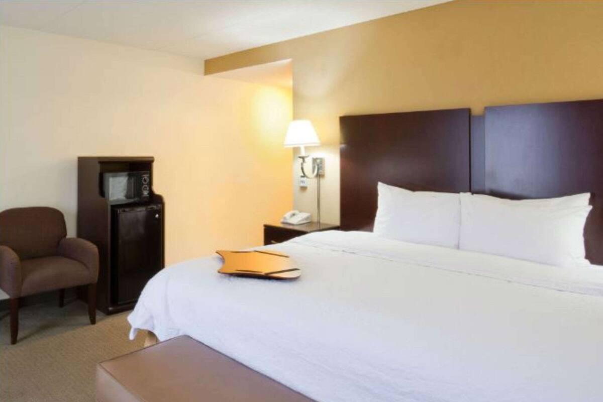 A hotel room with a large bed, a bedside table, a lamp, a chair, and a small desk.