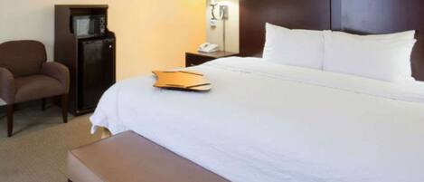 A hotel room with a large bed, a bedside table, a lamp, a chair, and a small desk.