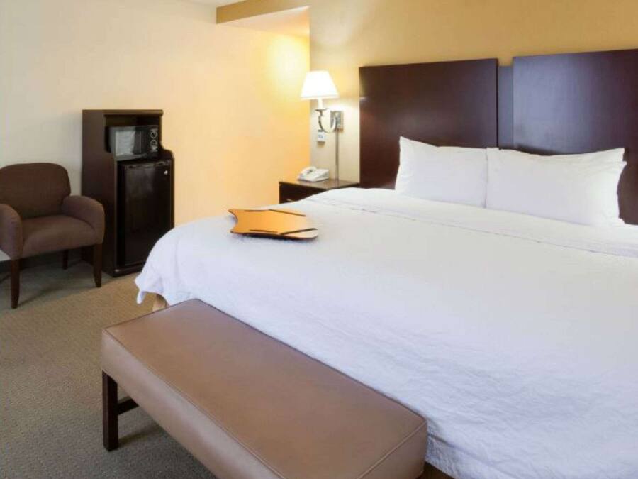 A hotel room with a large bed, a bedside table, a lamp, a chair, and a small desk.