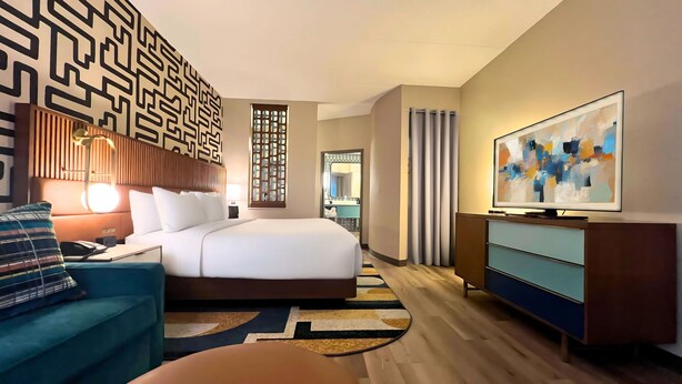 A modern hotel room with a large bed, a desk, a chair, a TV, and a decorative wall panel. - Hotel Indigo Columbus Architectural Center by IHG (Columbus)
