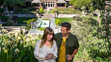 Una pareja parada en un jardín con una fuente y un césped bien cuidado.