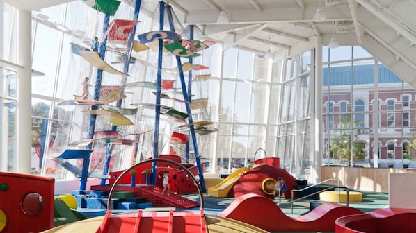 A children's play area with colorful play structures and a large window providing a view of a building outside. - Hotel Indigo Columbus Architectural Center by IHG (Columbus)