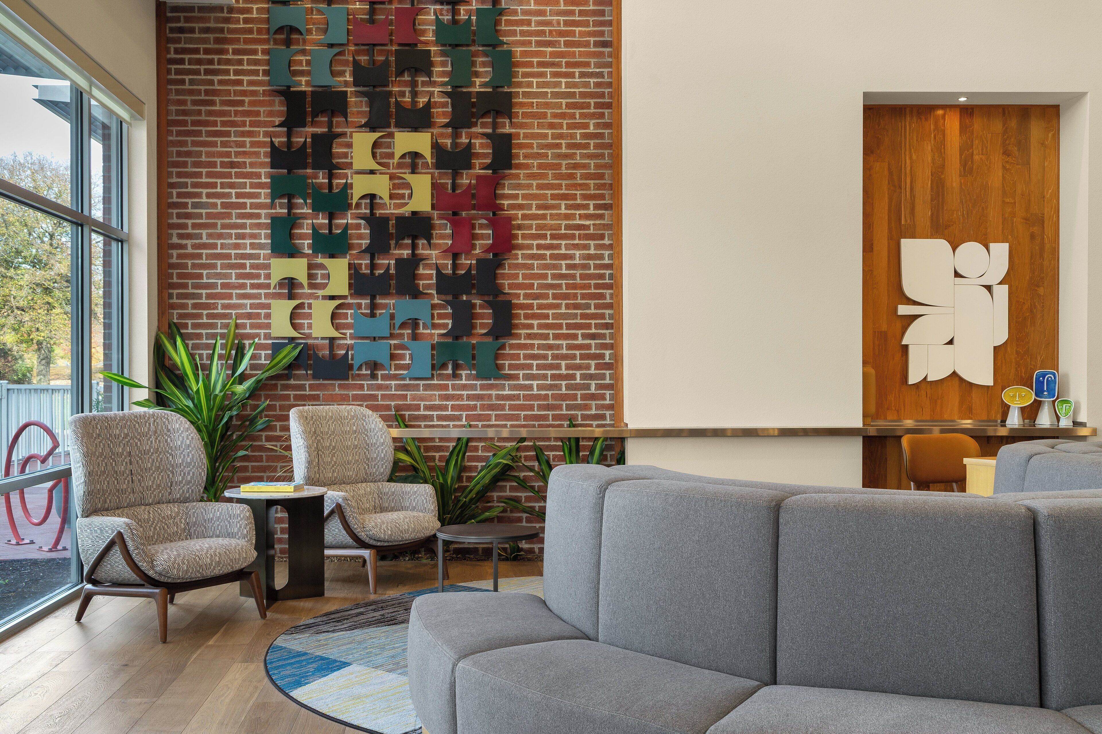 A modern lobby with a brick wall, two armchairs, a grey sofa, and a wooden reception desk.
