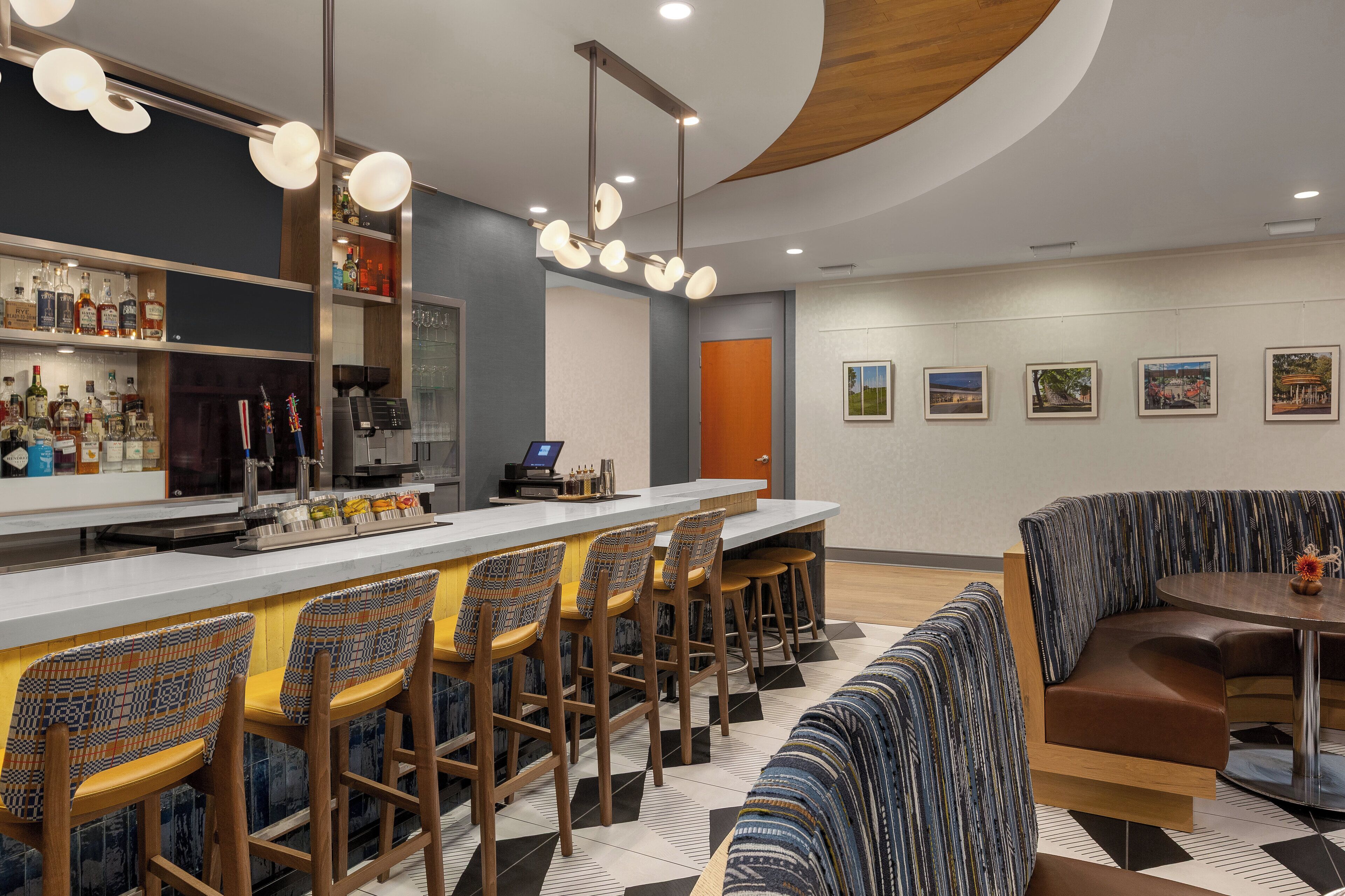 A modern bar area with a bar counter, stools, and a seating area with a round table and cushioned benches.