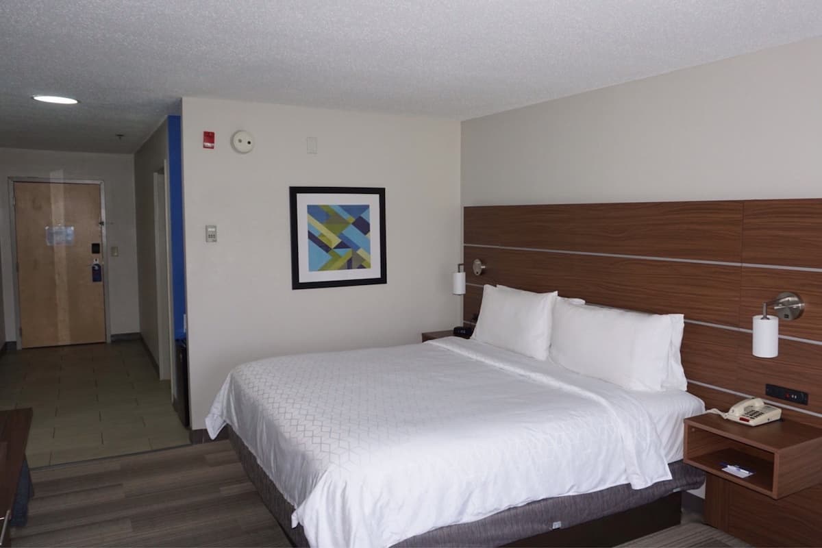 Une chambre d’hôtel avec un grand lit, une tête de lit en bois, une table de chevet avec un téléphone et un tableau encadré au mur.