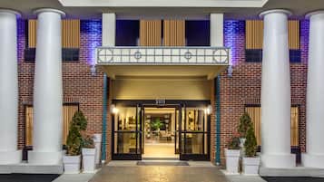Classic hotel entrance with a brick exterior and white columns, flanked by potted plants.