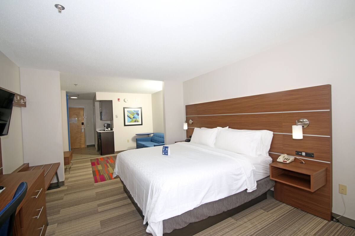 Une chambre d’hôtel avec un grand lit, un bureau, une chaise, une télévision et une salle de bain visible au fond.