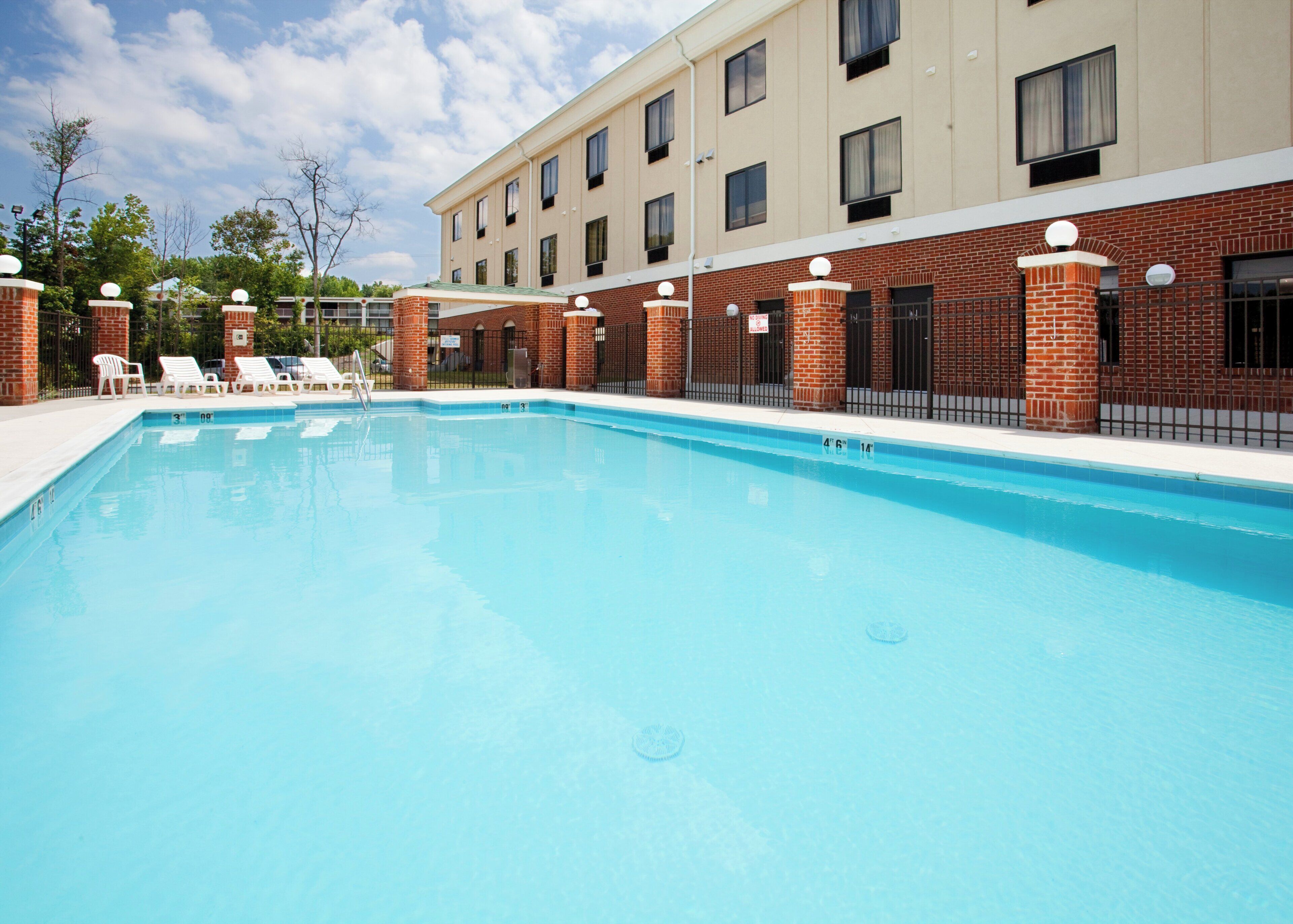 A rectangular swimming pool with a clear blue surface, surrounded by a brick building with multiple windows and a flat roof.