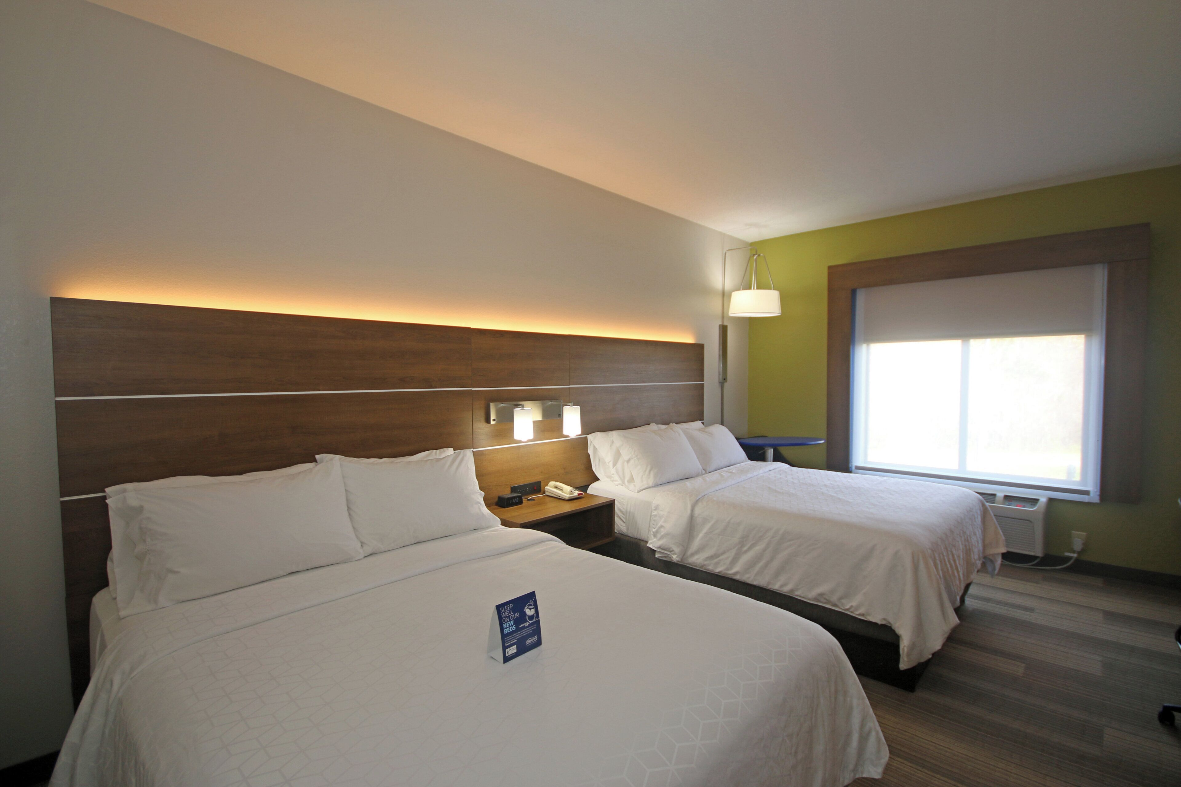 A hotel room with two beds, a nightstand with a phone, and a window with blinds.