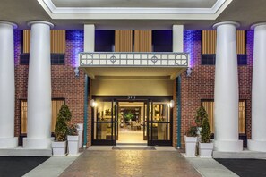 L’entrée d’un hôtel, avec une façade en briques, de grandes colonnes et un balcon agrémenté de balustrades décoratives.