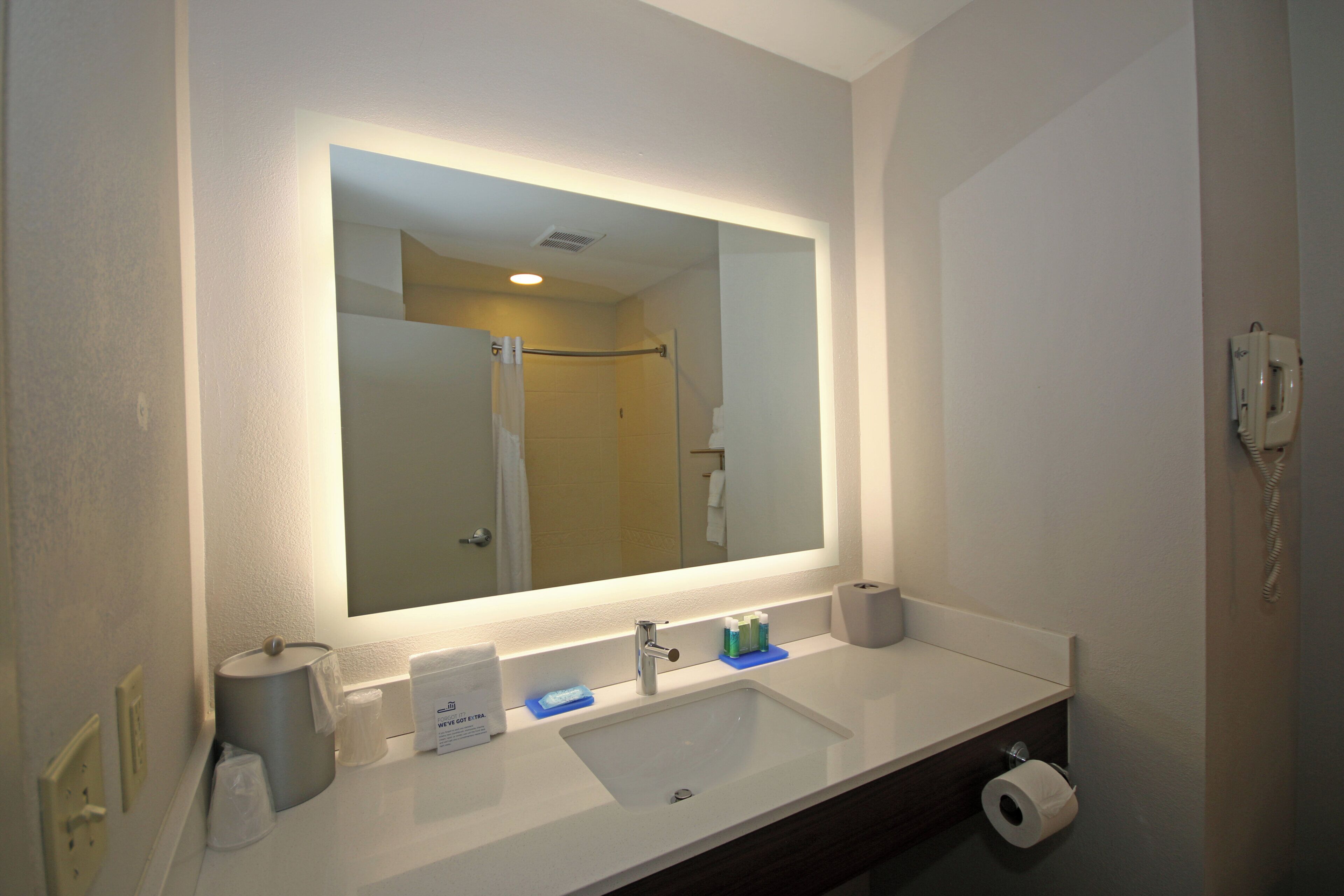 A bathroom with a large mirror, a sink, a toilet, and a telephone.