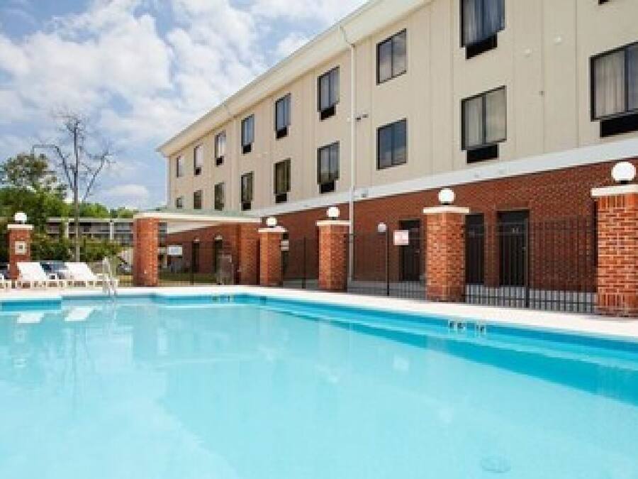 A swimming pool with lounge chairs and a building with multiple windows and brick pillars.