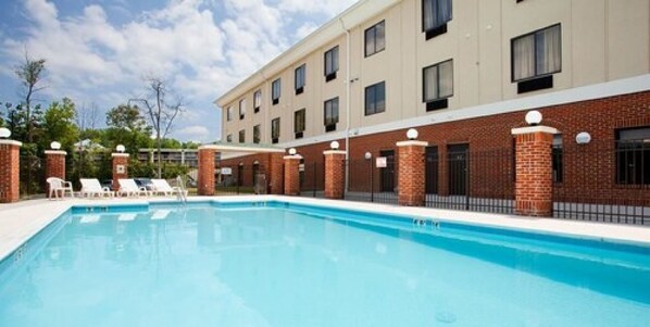 Una piscina con sillas de descanso y un edificio con varias ventanas y pilares de ladrillo.