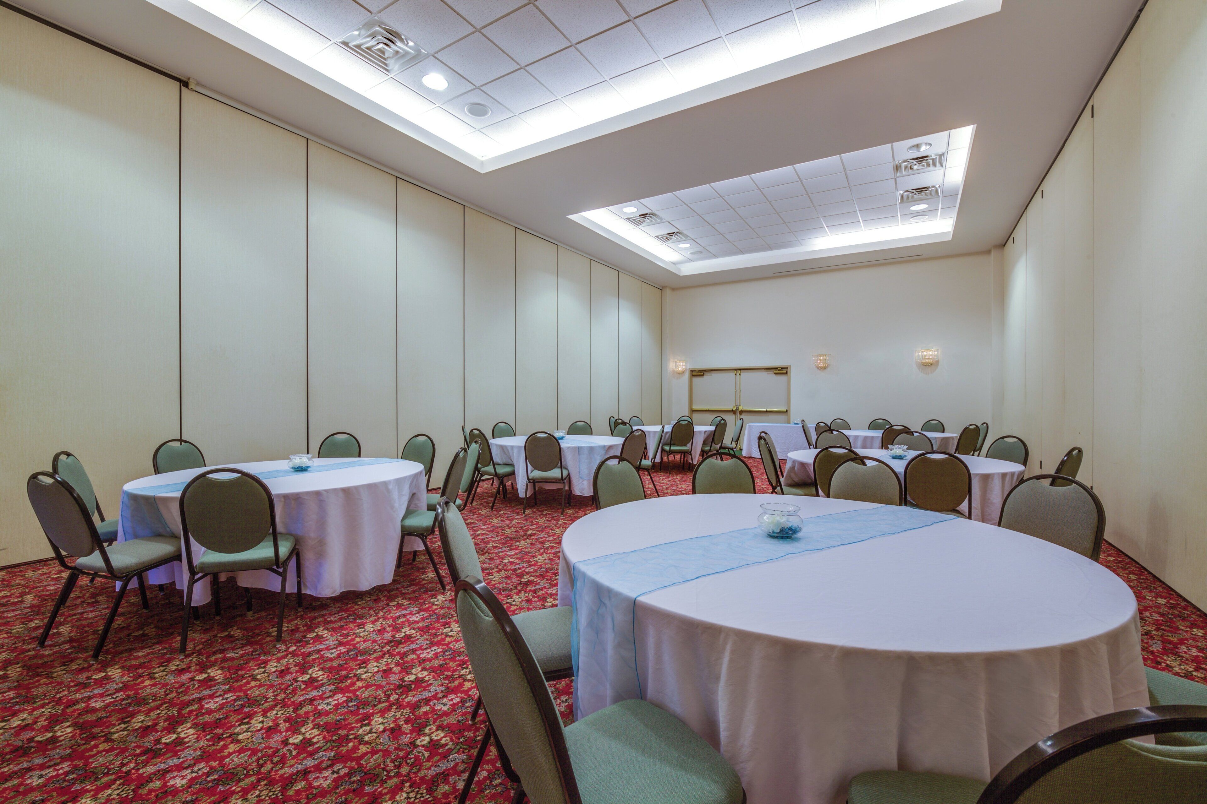A conference room with multiple round tables, chairs, and a carpeted floor.