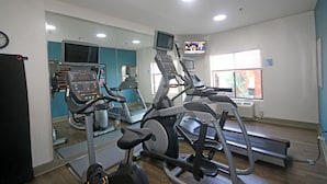 Ein Fitnessraum mit verschiedenen Trainingsgeräten, einem Fernseher und einer Uhr an der Wand.