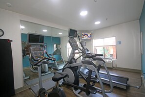 A gym with various exercise equipment, a television, and a clock on the wall. - Holiday Inn Express Hotel & Suites Greensboro - East by IHG (Greensboro)