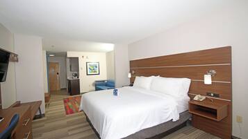 Une chambre d’hôtel avec un grand lit, un bureau, une chaise, une télévision et une salle de bain visible au fond.