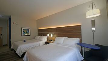 A hotel room with two beds, a bedside table with a lamp, a small desk, and a chair.