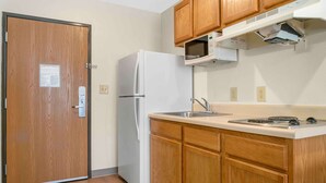 A compact kitchen with wooden cabinets, a white refrigerator, a microwave, and a sink.