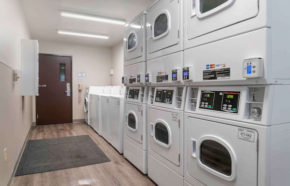Un cuarto de lavandería con varias lavadoras apiladas, una puerta y un panel de control.
