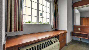 A room with a window, a desk with drawers, a heater, and a mirror.