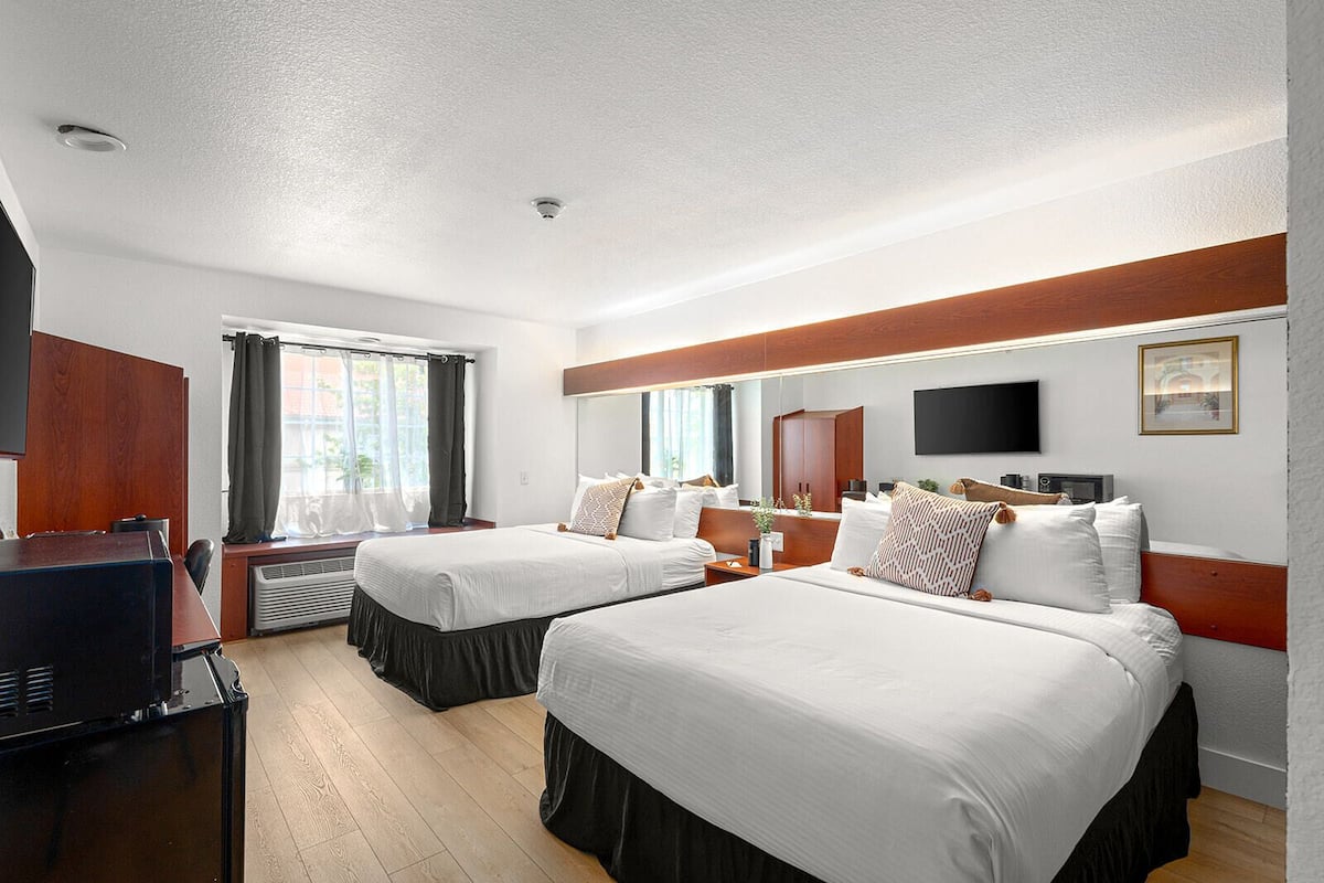 A hotel room with two beds, a TV, a desk, and a window with curtains.