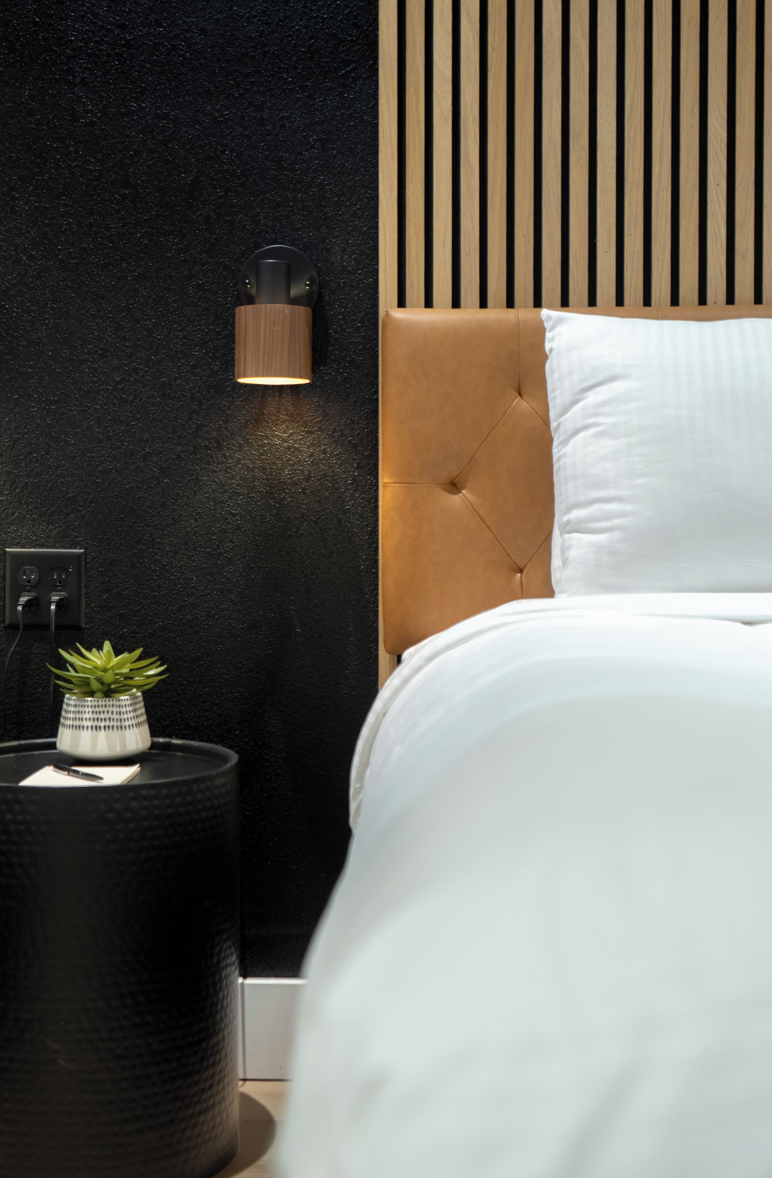 A modern bedroom with a tufted headboard, a bedside table with a plant, and a wall-mounted light fixture.