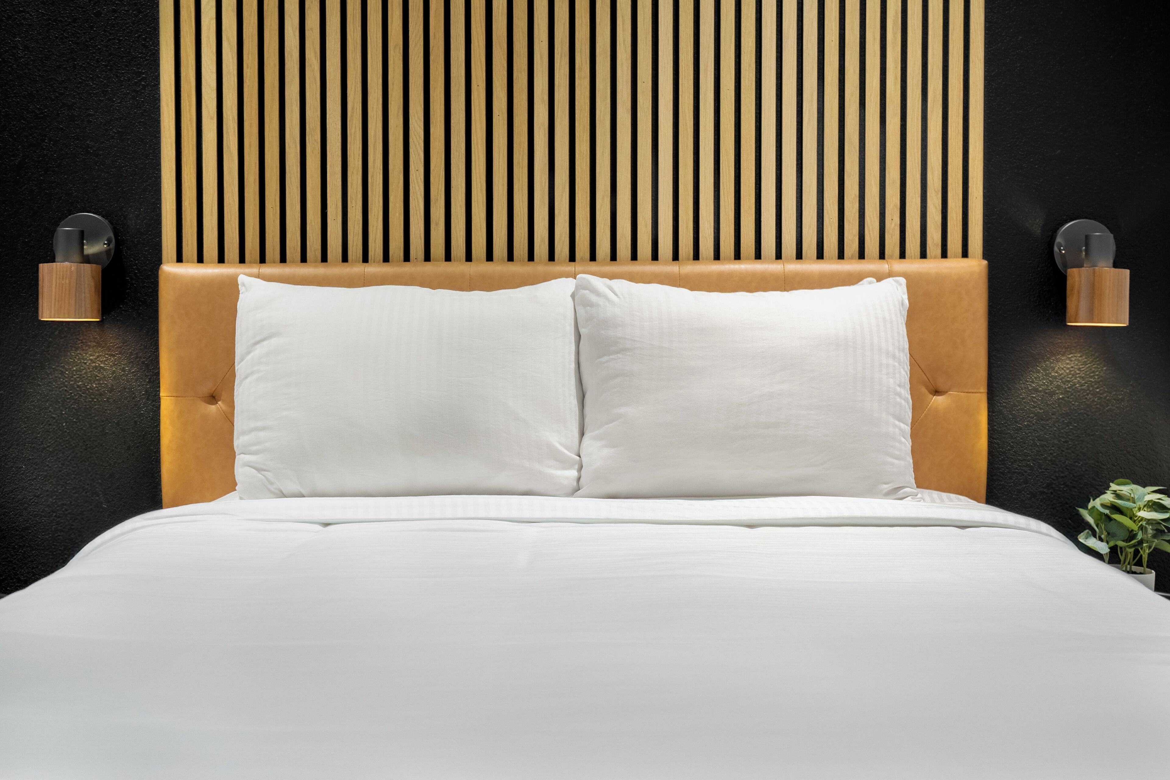 A bed with a wooden headboard, two white pillows, and two wall-mounted light fixtures on either side.