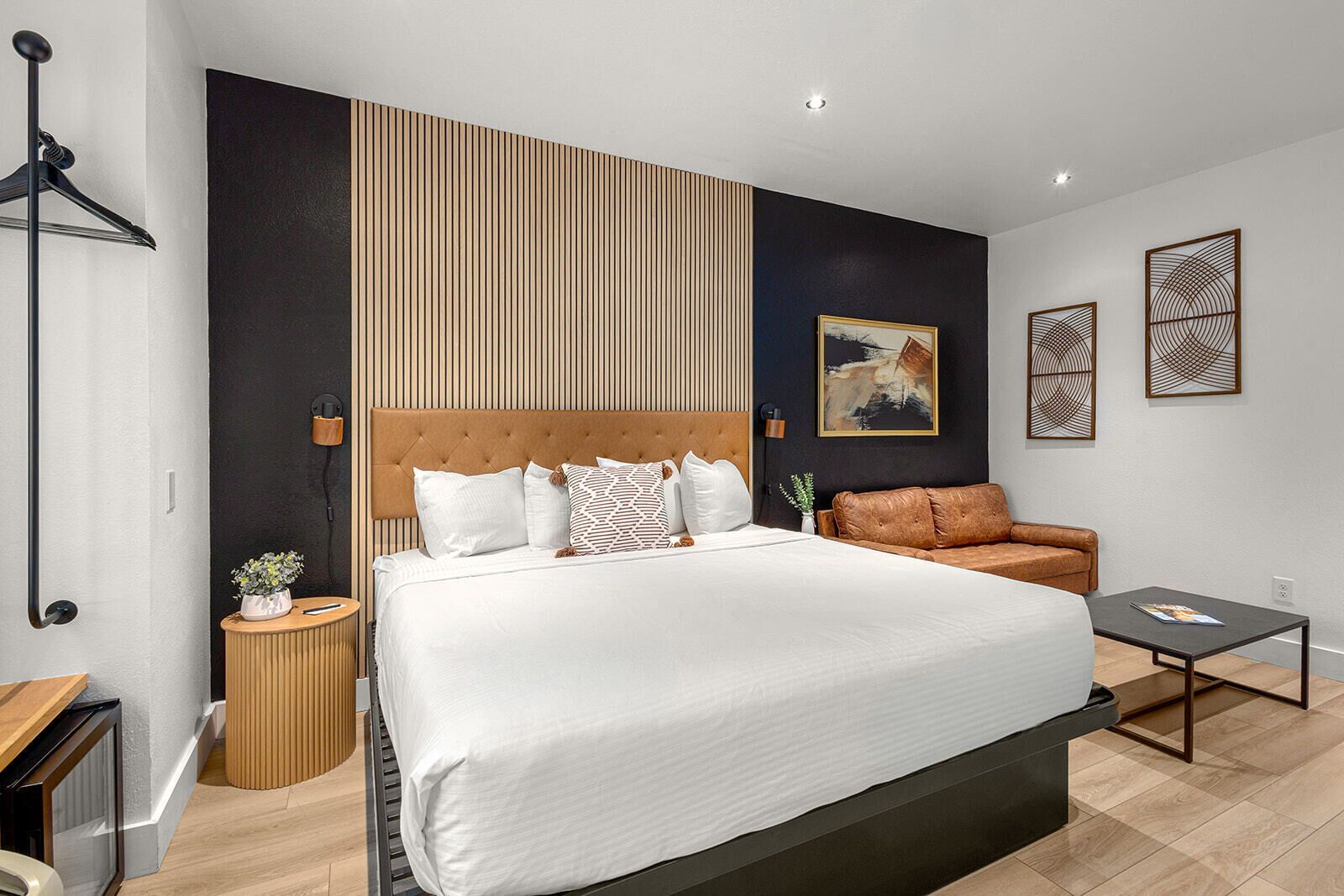 A modern hotel room with a large bed, a sofa, a small table, and a wall-mounted shelf.