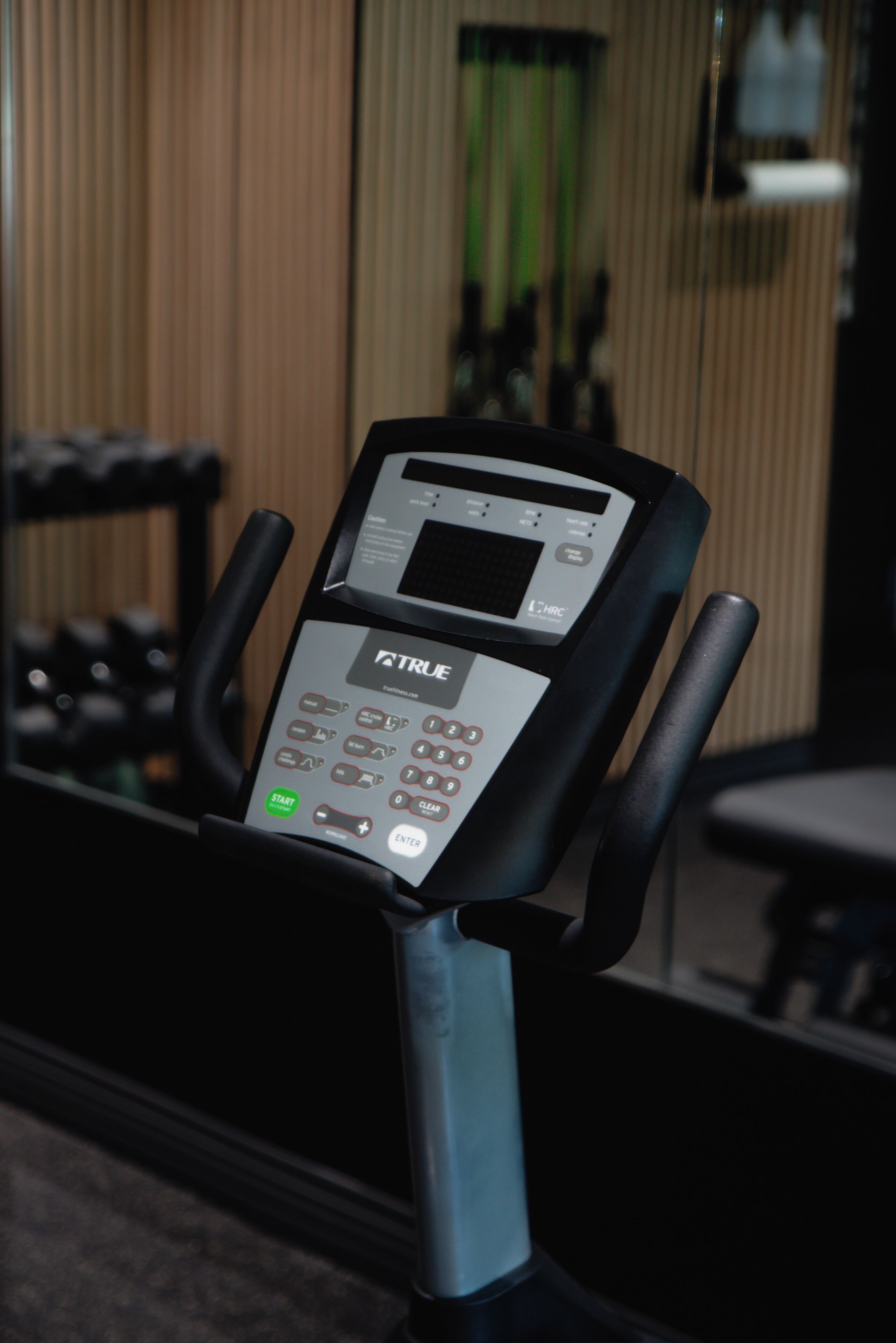 A stationary exercise bike with a digital display and control panel, positioned in a room with a window and blinds.